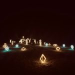 Naktinė scena su dekoratyviniais šviesos elementais, išdėstytais ant žemės.